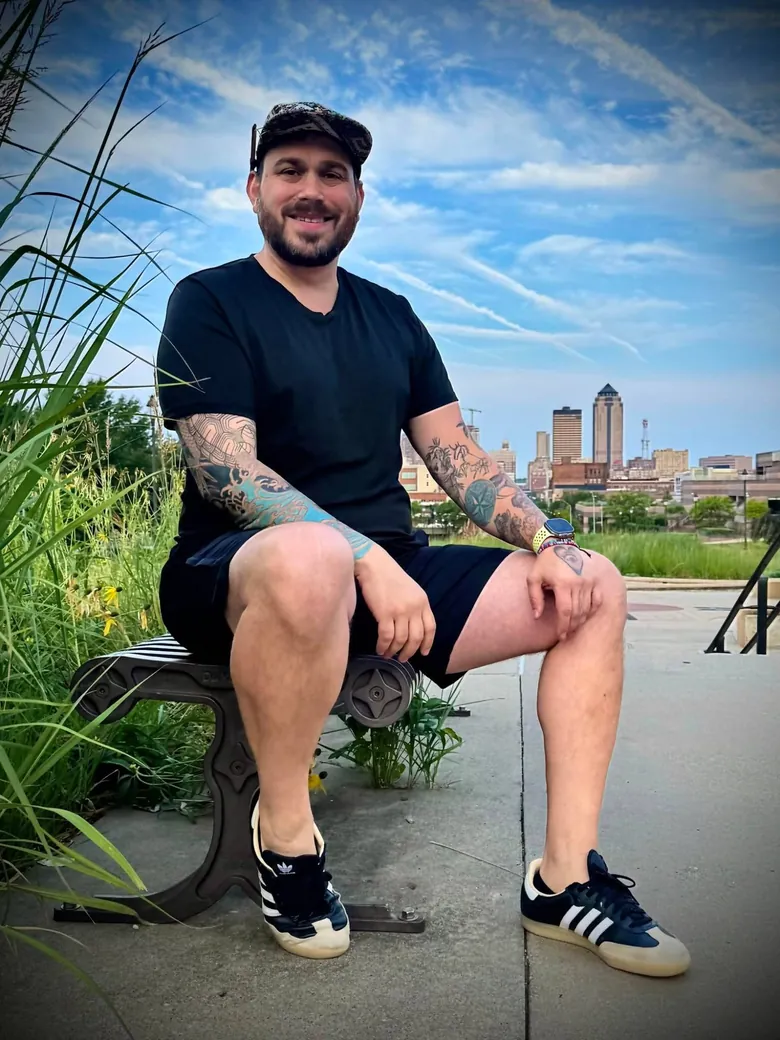 Ben sitting on a bench with the Des Moines skyline behind him