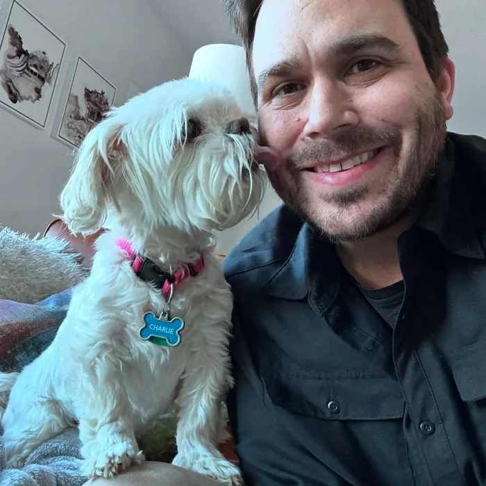 Ben indoors with Charlie, a small white dog, on his shoulder